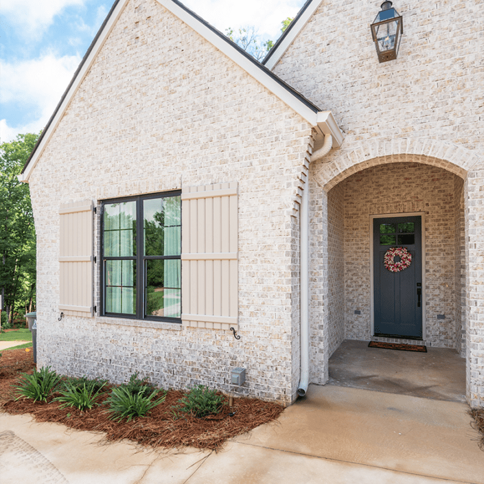 Board and Baten exterior shutters built by Dwell Shutter & Blinds displayed on a brick house.